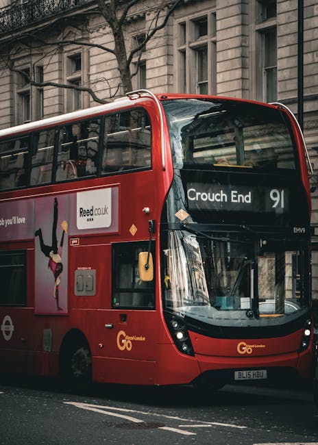 A red double-decker bus parked on a city street with tall, historic buildings in the background. The bus displays the destination 'Crouch End' and route number 91 on the front, with visible windows reflecting surrounding structures. The exterior of the bus features advertising artwork and company logos, with a sleek, glossy finish. The scene is bathed in natural daylight, highlighting the bus's vibrant color and the urban environment. Cleaner Haringey specializes in professional cleaning services for residential and commercial spaces, ensuring hygiene and cleanliness in your property.